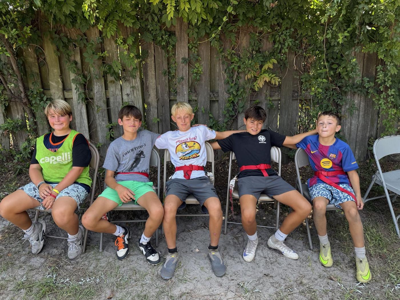 Five FAST kids in flag belts sitting together by the fence