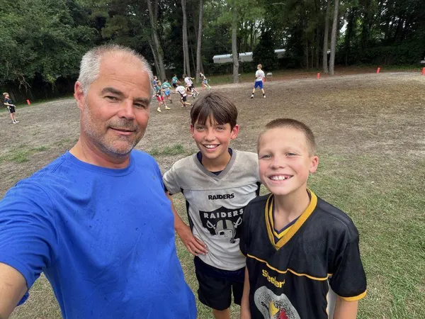 Coach Mike with two FAST kids, a flag football game behind them